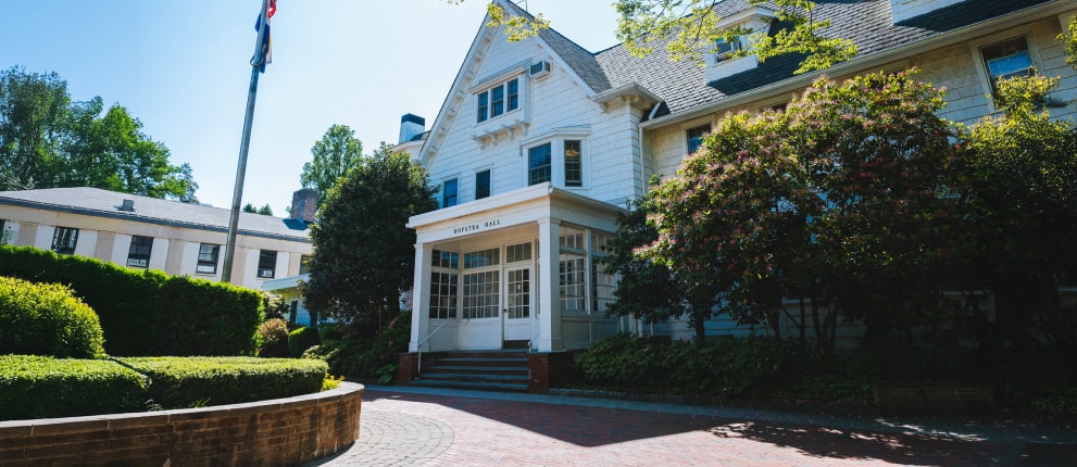 A large white house with a peaked roof and many windows, surrounded by shrubs and trees, with a brick path and steps leading to a sunlit entrance labeled POTTER HALL.